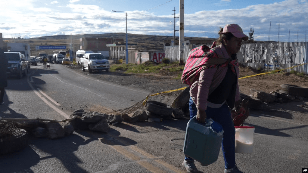 Una mujer cargada con contenedores llenos de leche atraviesa caminando los bloqueos de carretera colocados por los manifestantes de oposición al gobierno en la carretera de Juliaca, sur de Perú, a Puno, Bolivia, el viernes 10 de marzo de 2023.
