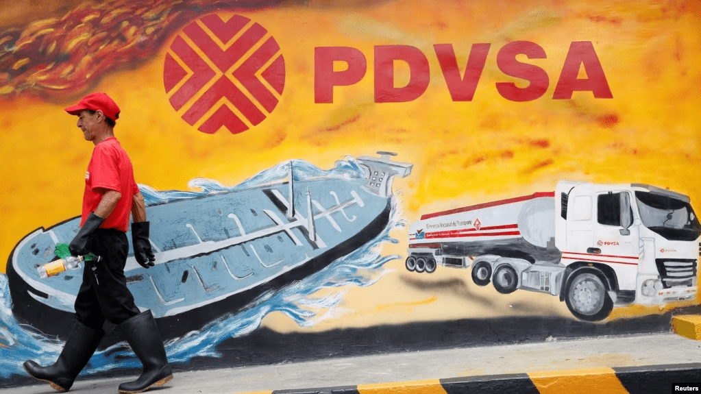 Un empleado de una estación de servicio de Caracas pasa frente a un mural con el logo de la estatal petrolera PDVSA, en agosto de 2014.