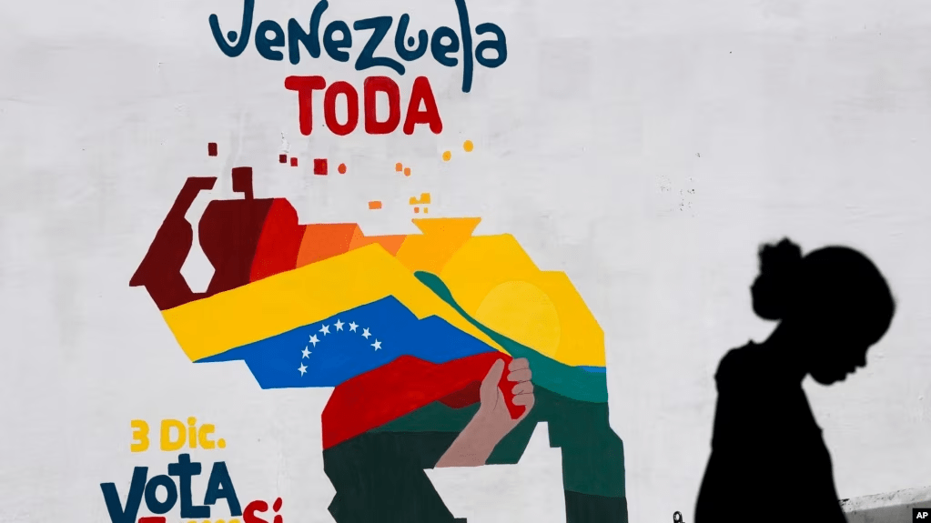 Una mujer vende frutas frente a un mural con el mapa de Venezuela donde se promueve la participación pro oficialista en el referendo consultivo del domingo, en Caracas, el 29 de noviembre de 2023.