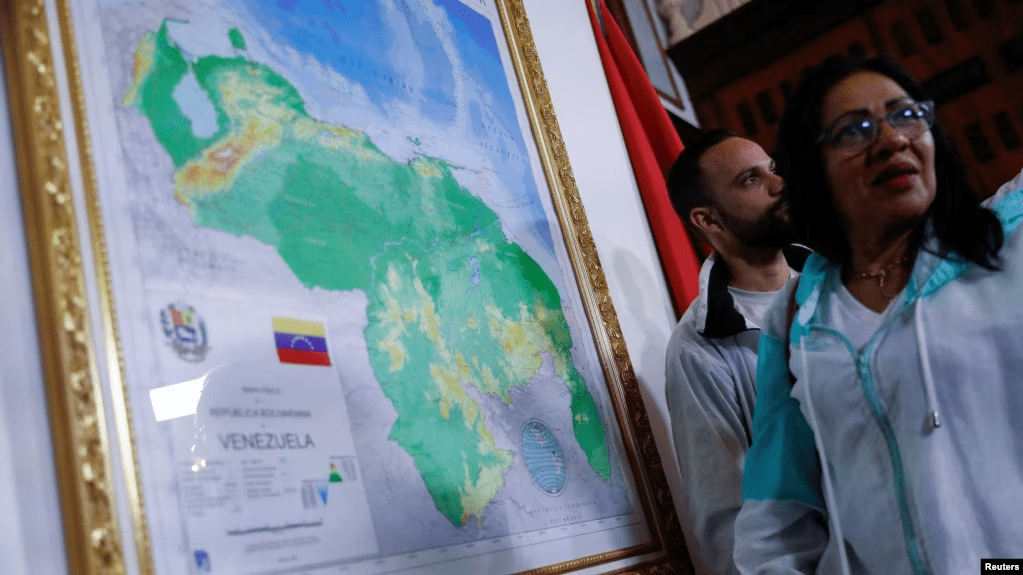 Dos personas conversan cerca de un mapa enmarcado de Venezuela, promovido por el gobierno de Nicolás Maduro para anexar un nuevo estado, el Guayana Esequiba, en Caracas, el 8 de diciembre de 2023.